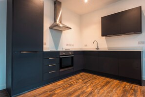 Une cuisine moderne avec des meubles de couleur sombre, une hotte de cuisinière en acier inoxydable et un plancher en bois.
