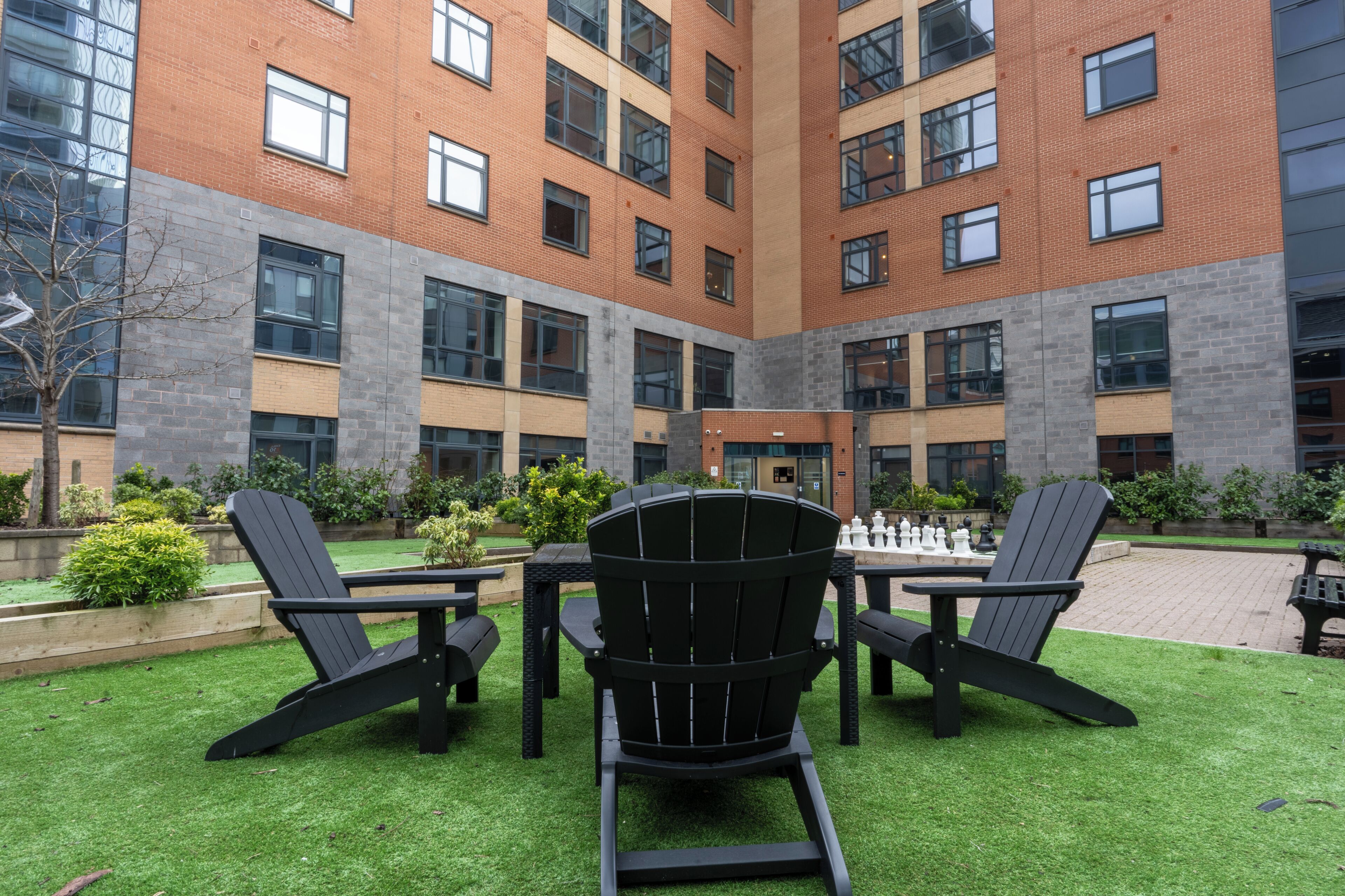 A courtyard with a brick building, outdoor seating, and a chess table.
