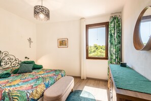 Un dormitorio con cama, un banco, una ventana con cortinas, una lámpara colgante y un cuadro en la pared.