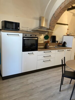 A modern kitchen with white cabinetry, a built-in oven, a microwave, and a brick archway. - La Casa Di Memmo in the Heart of the Sienese Countryside (Petroio)