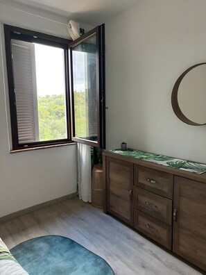 A room with a large window, a wooden cabinet with drawers, a round mirror, and a blue rug. - La Casa Di Memmo in the Heart of the Sienese Countryside (Petroio)