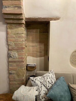 A room with a brick fireplace, a sofa, and a side table with books. - La Casa Di Memmo in the Heart of the Sienese Countryside (Petroio)