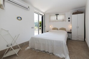 A bedroom with a bed, a wardrobe, a small table, and a hanging light fixture. - Villa Ninfea - Capri Garden Retreat (Capri)