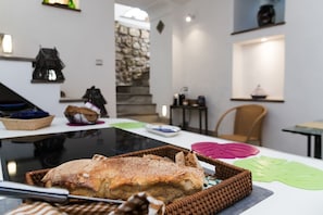 A dining area with a table set for a meal, a wicker basket with bread, and a stone wall in the background. - Villa Ninfea - Capri Garden Retreat (Capri)