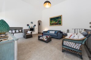 A living room with a sofa, coffee table, wicker chair, and a painting on the wall. - Villa Ninfea - Capri Garden Retreat (Capri)