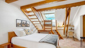 Une chambre avec un lit en bois, une lucarne, un escalier en bois et une vue sur l’extérieur.