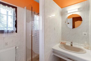 Ein Badezimmer mit Dusche, Waschbecken, Spiegel und einem Fenster mit Spitzenschleier.