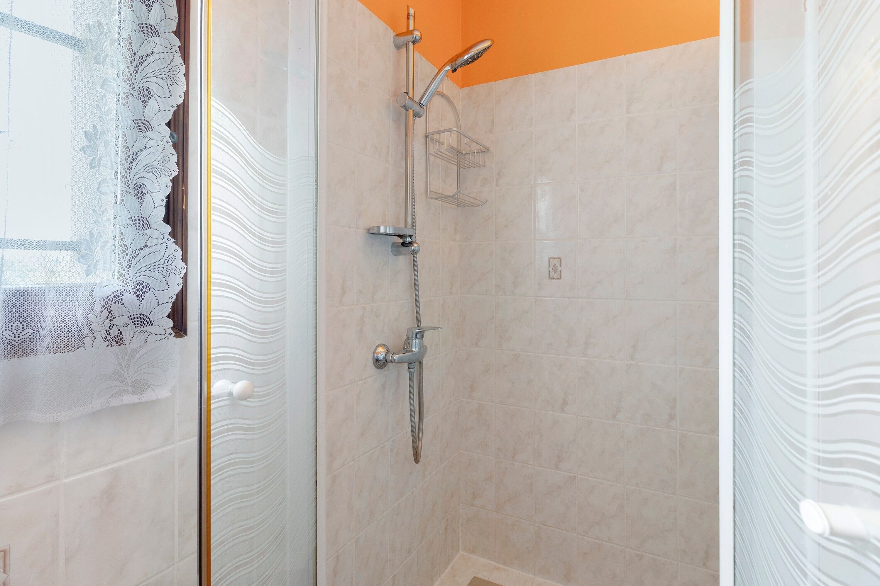 A shower with a chrome faucet, a handheld showerhead, and a wall-mounted shelf.
