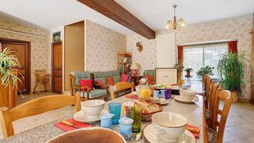 Un coin repas avec une table en bois dressée pour le petit-déjeuner, entourée de chaises, et une bibliothèque en arrière-plan.