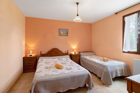 Une chambre avec deux lits, des tĂȘtes de lit en bois, des tables de chevet avec des lampes, un tableau au mur et une fenĂȘtre donnant sur un paysage.