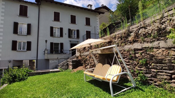 A patio with a swing chair, a stone wall, and a building with multiple windows and balconies. - House with Garden and Terrace (Gurro)