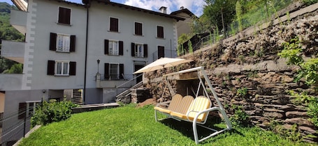 A patio with a swing chair, a stone wall, and a building with multiple windows and balconies.. House with Garden and Terrace