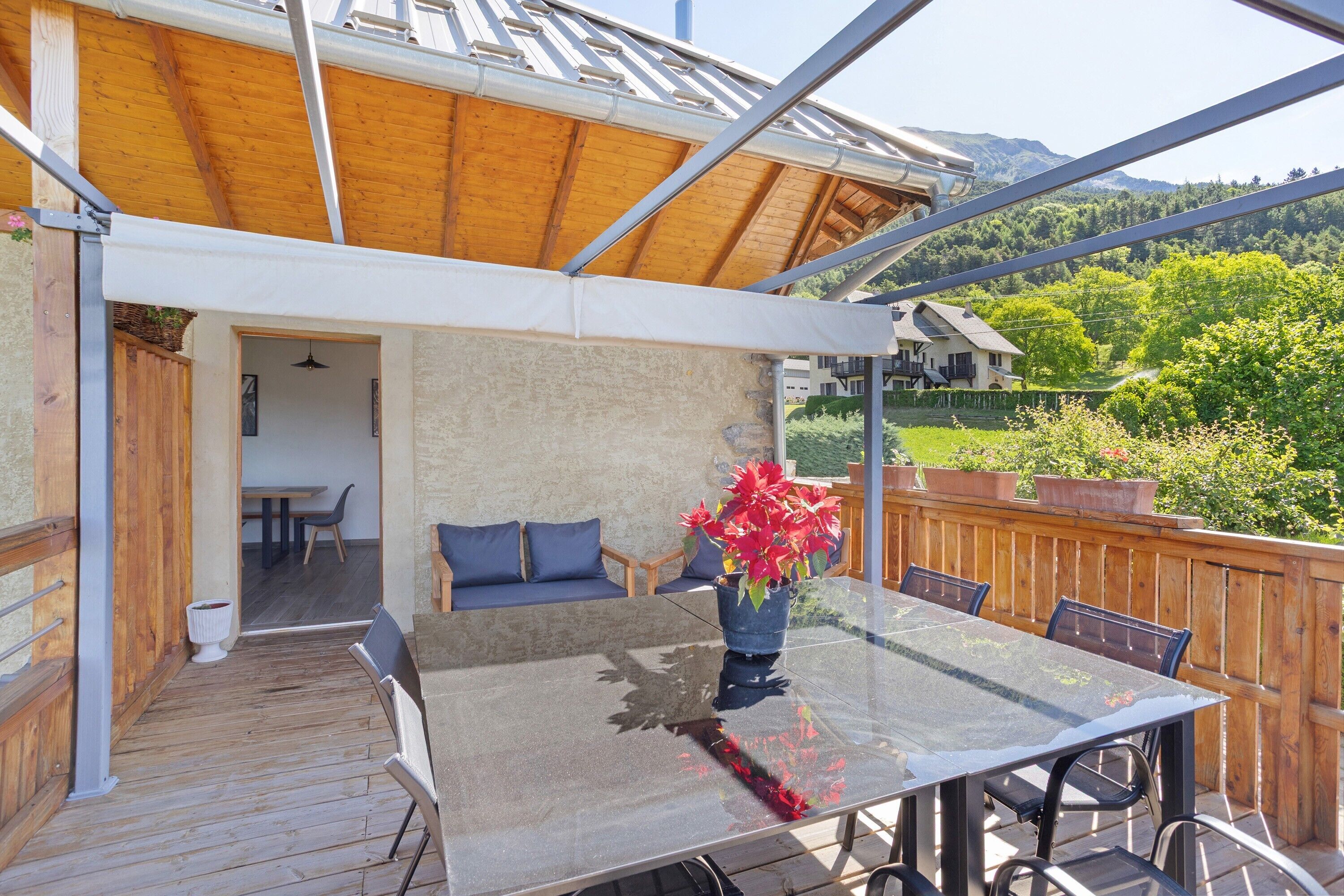Une terrasse extérieure couverte, dotée d’une table et de chaises en verre, d’une clôture en bois et offrant une vue sur une montagne.