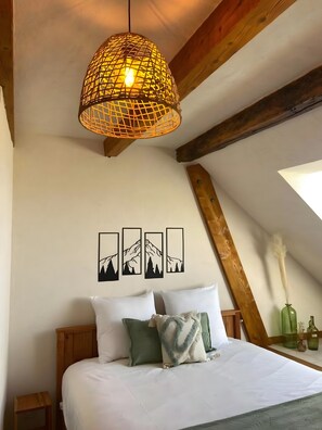 A bedroom with a bed, pillows, a hanging light fixture, and wall art.