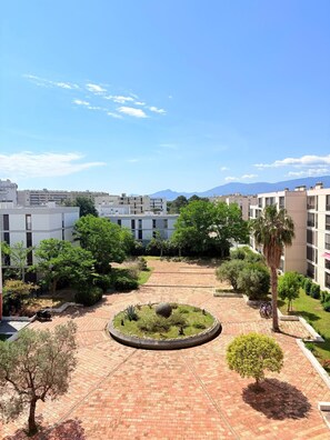 Ein Innenhof mit einem kreisförmigen Garten, umgeben von Gebäuden mit Balkonen und Blick auf die Berge im Hintergrund.