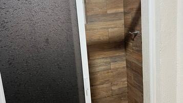 Baño con zona de ducha, paredes de madera y una puerta negra con textura.
