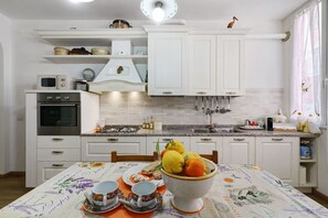 Una cocina con armarios blancos, una estufa, un microondas y un frutero sobre la mesa.