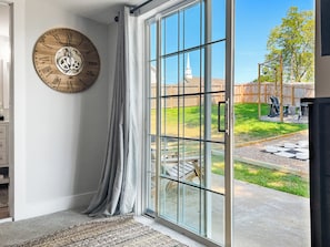 A room with a large wooden clock, a sliding glass door leading to an outdoor area with a wooden fence and a checkered pattern on the ground.