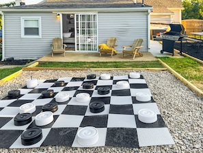 A checkered outdoor area with a grill and chairs, a small shed, and a house in the background.