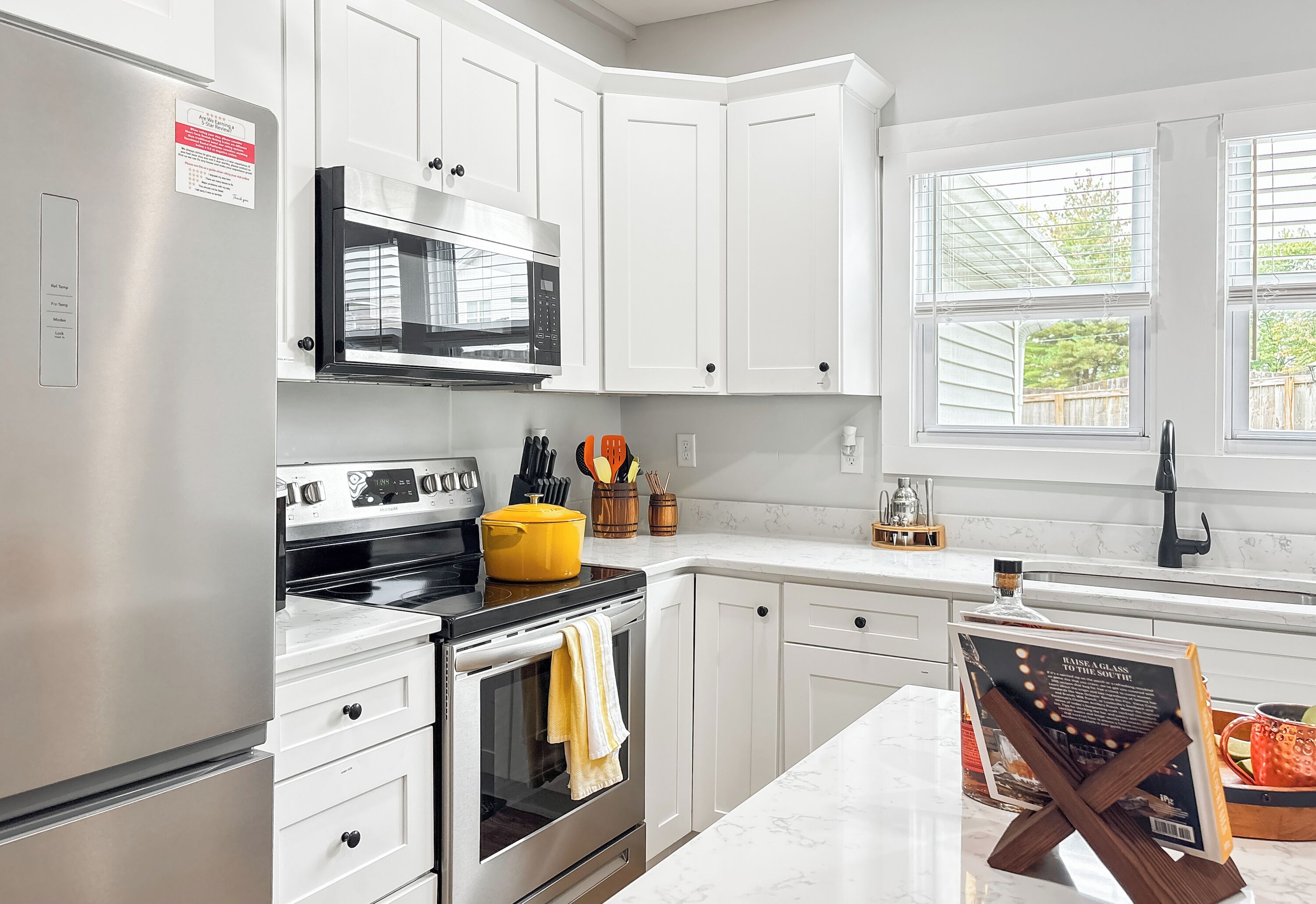 A modern kitchen with white cabinets, stainless steel appliances, a microwave, and a yellow pot on the stove.