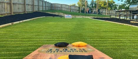 A wooden table with a hole in the center, surrounded by a grassy area with a wooden fence in the background.
