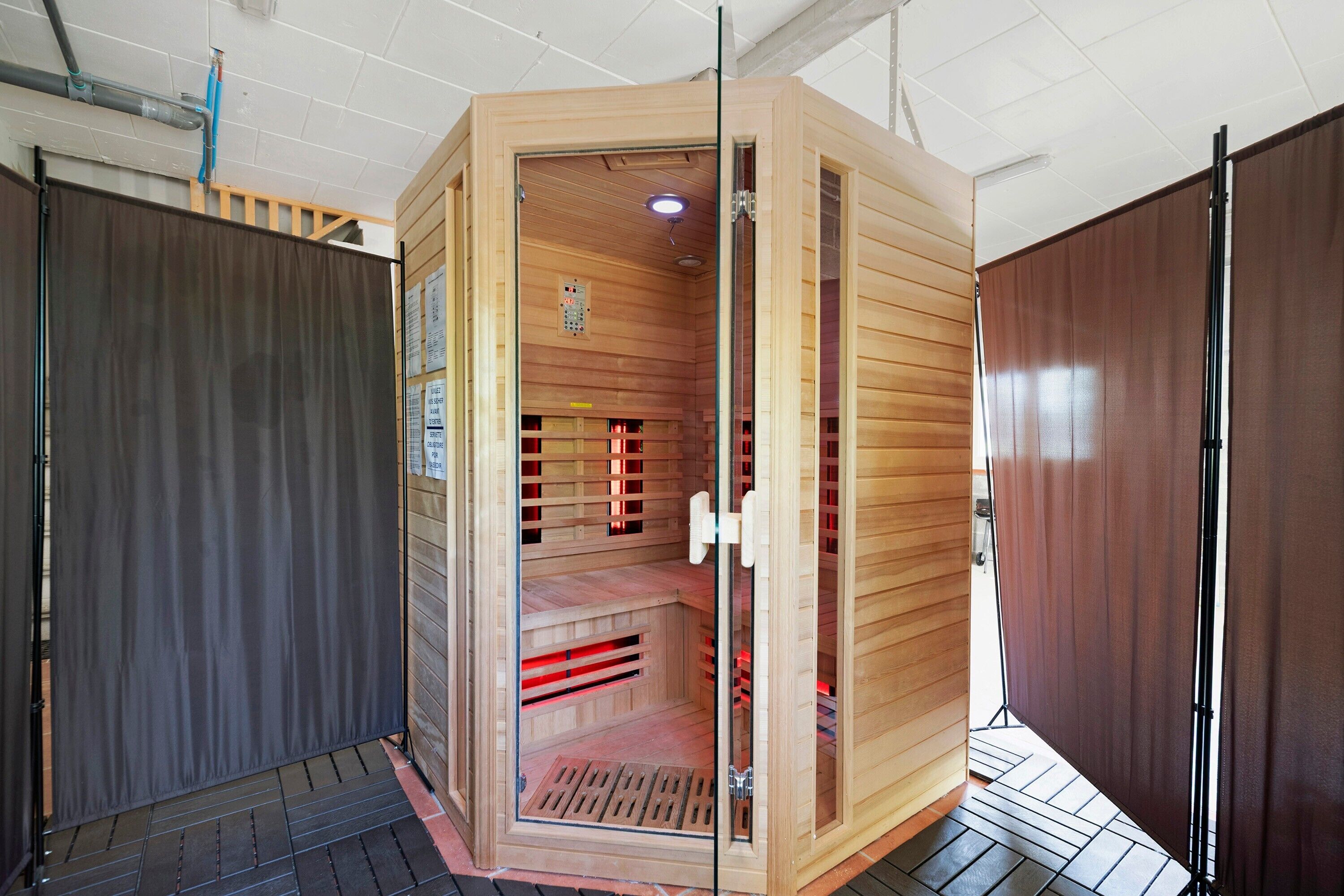 A sauna with a glass door, wooden interior, and a control panel.