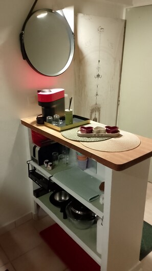 Uma kitchenette compacta com cafeteira, chaleira e um pequeno armário com utensílios de cozinha.