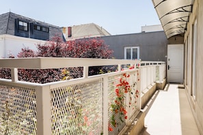 A narrow outdoor corridor with a white fence, red flowering plants, and a door at the end. - Terranova Apartments by Andes STR (Providencia)
