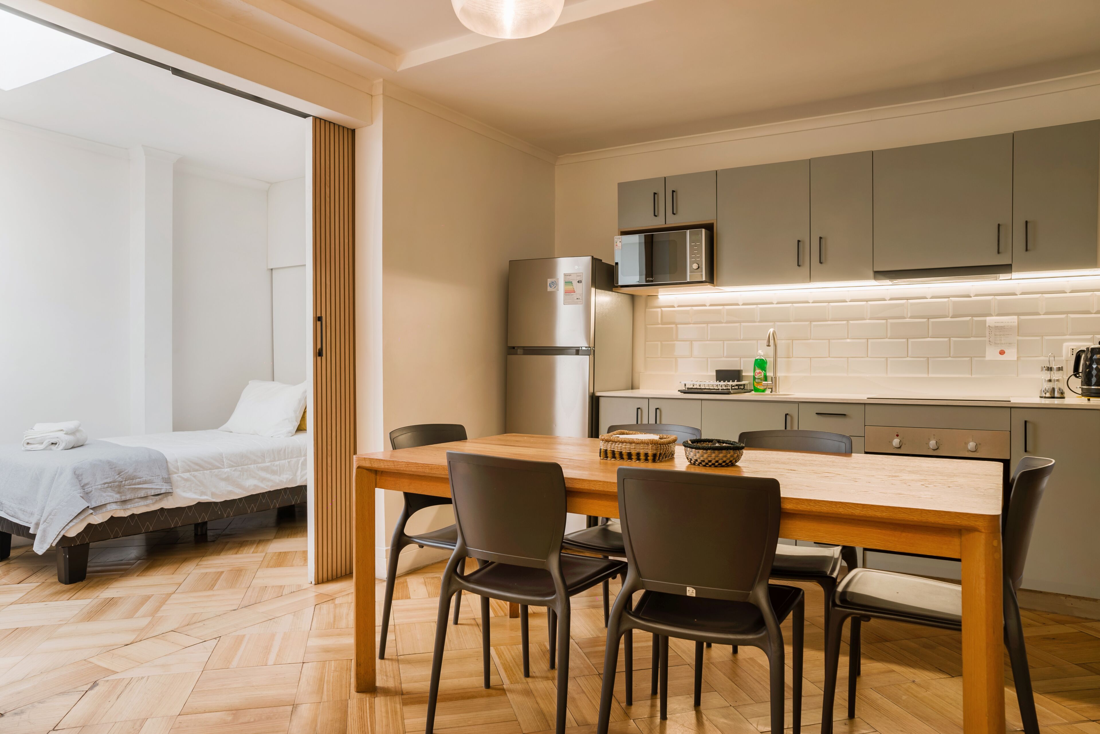 A compact kitchen with a refrigerator, microwave, and a wooden dining table with chairs.