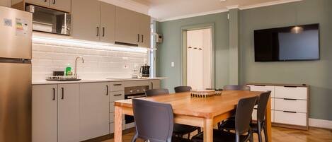 A modern kitchen with a dining table and chairs, a microwave, and a flat-screen TV mounted on the wall.
