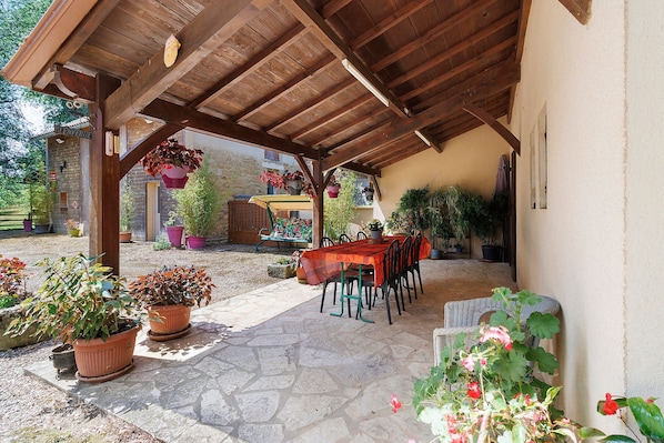 A covered patio with a stone floor, wooden ceiling, and a table with chairs.