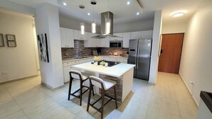 A modern kitchen with a central island, bar stools, stainless steel appliances, and a tiled floor. - Isabela Jardin • Cozy Luxe Stay • 3BR • Pool + AC (Isabela)