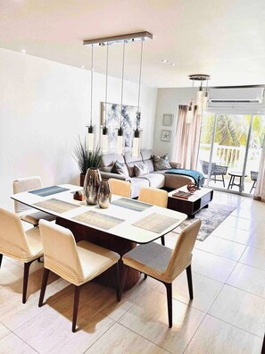 A modern living room with a dining area, featuring a sofa set, a coffee table, and hanging pendant lights. - Isabela Jardin • Cozy Luxe Stay • 3BR • Pool + AC (Isabela)
