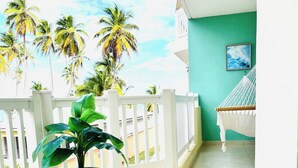 A balcony with a potted plant, a hammock, and a view of palm trees. - Isabela Jardin • Cozy Luxe Stay • 3BR • Pool + AC (Isabela)