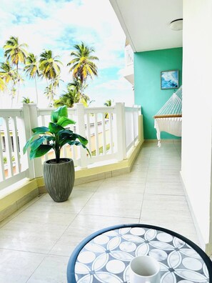 A balcony with a potted plant, a hammock, and a view of palm trees. - Isabela Jardin • Cozy Luxe Stay • 3BR • Pool + AC (Isabela)