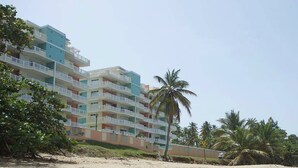 A beachfront hotel with multiple balconies, palm trees, and a sandy beach. - Isabela Jardin • Cozy Luxe Stay • 3BR • Pool + AC (Isabela)