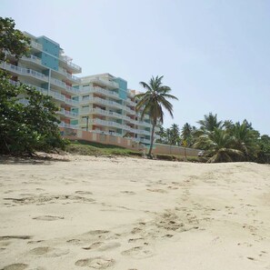 A beachfront hotel with multiple balconies, palm trees, and a sandy beach. - Isabela Jardin • Cozy Luxe Stay • 3BR • Pool + AC (Isabela)