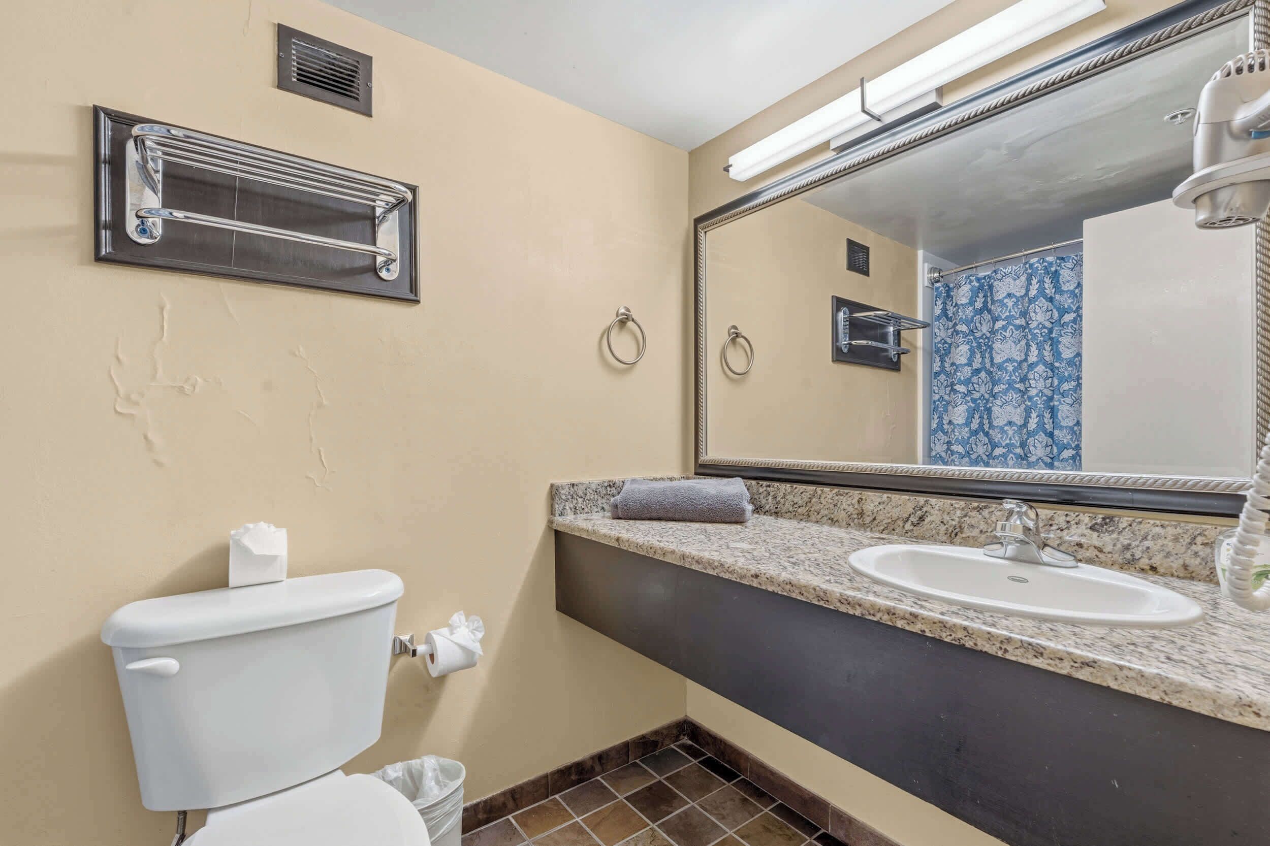 Baño con inodoro, lavamanos, toalleros y espejo.