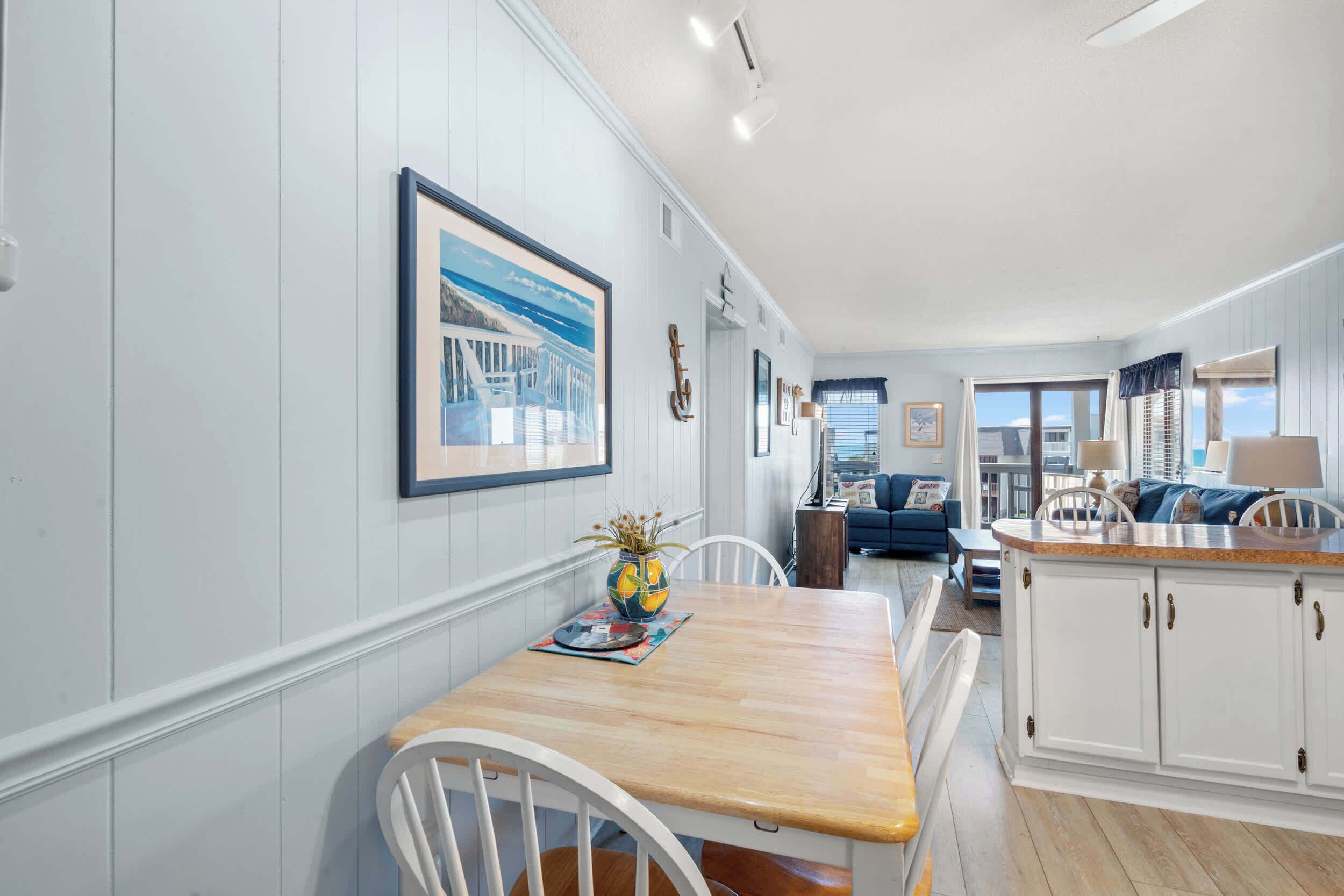 Een eetgedeelte met een houten tafel en stoelen, een keuken met witte kasten en een woonkamer met een blauwe bank.