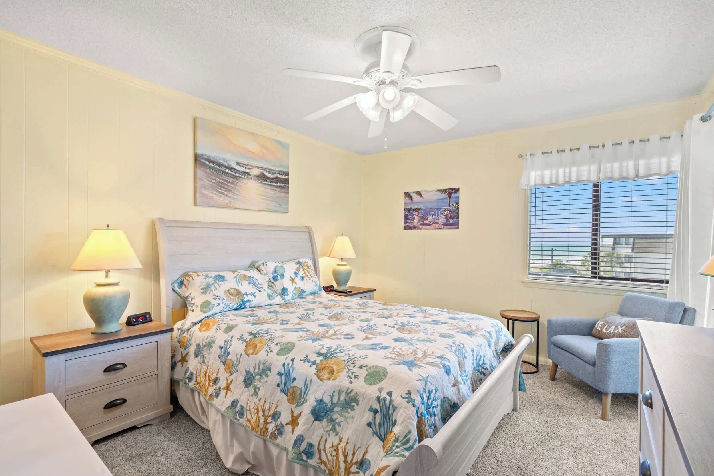 A bedroom with a bed, nightstands, a chair, a ceiling fan, and a window with blinds.