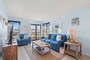 Ein Wohnzimmer mit zwei blauen Sofas, einem Holztisch, einem Beistelltisch mit Lampe und einem an der Wand befestigten Schild.