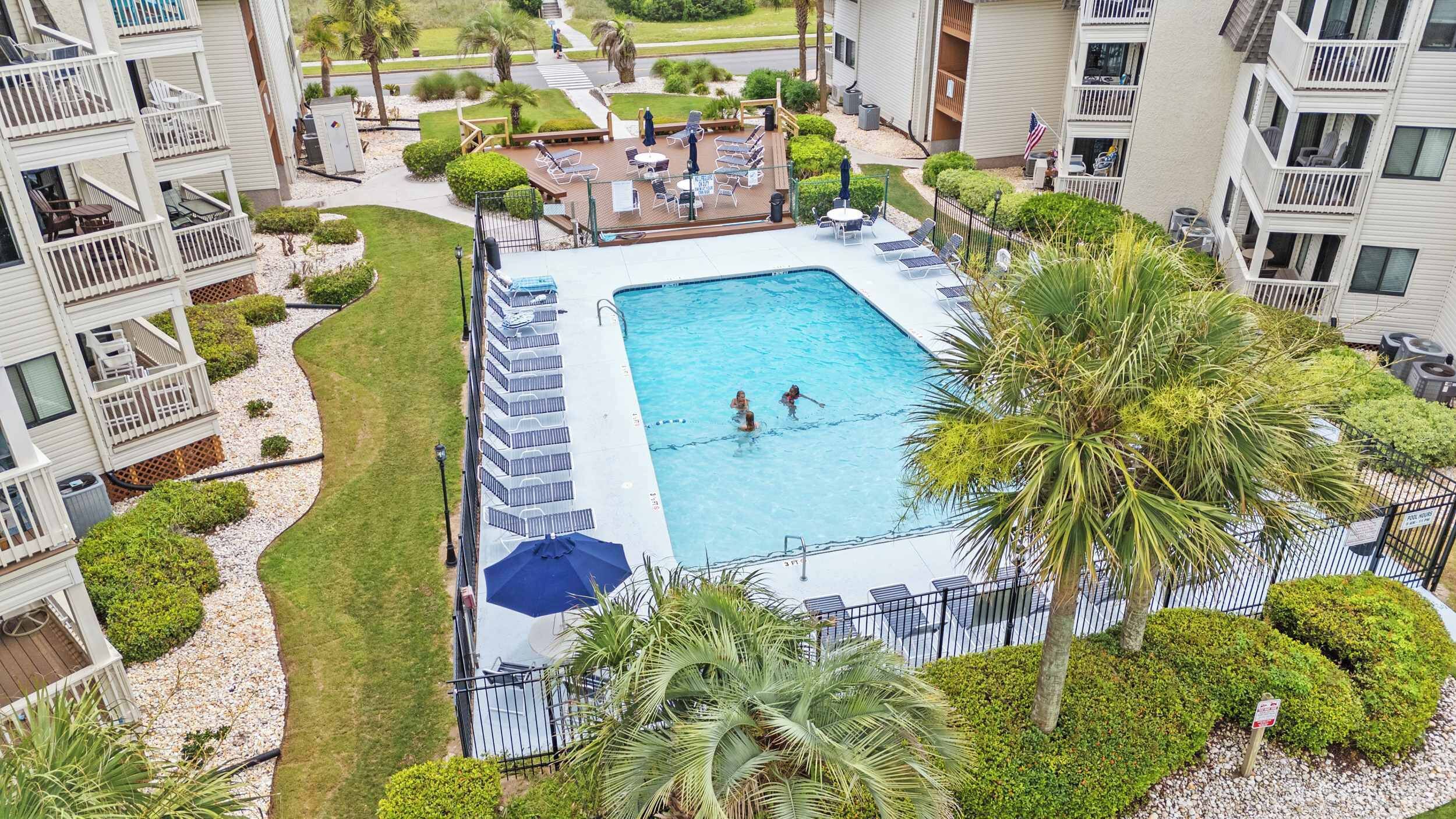 A swimming pool surrounded by a deck with lounge chairs, palm trees, and a view of apartment buildings.