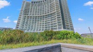 Ein Hochhaus-Hotel mit mehreren Balkonen, einem geschwungenen architektonischen Design und Blick auf die umliegende Grünfläche.