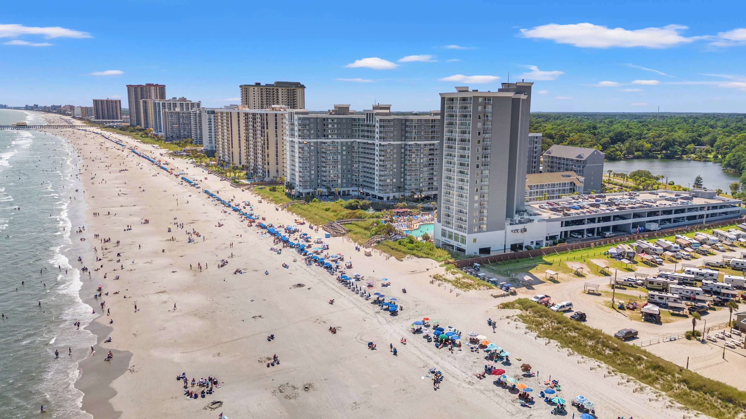 Un hôtel situé en bord de mer, composé de plusieurs immeubles de grande hauteur, doté d’une plage de sable et d’un parking.