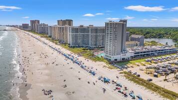 Un hôtel situé en bord de mer, composé de plusieurs immeubles de grande hauteur, doté d’une plage de sable et d’un parking.