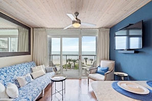 A room with a ceiling fan, a TV mounted on the wall, a sofa, a chair, a table, and a balcony with a view of the ocean. - SeaWatch 414 Ocean View (Myrtle Beach)