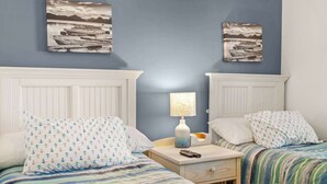 A room with two beds, a nightstand, a lamp, and two wall-mounted paintings. - "Seas the Day" at barefoot resort in Ironwood (North Myrtle Beach)