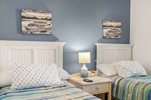 A room with two beds, a nightstand, a lamp, and two wall-mounted paintings. - "Seas the Day" at barefoot resort in Ironwood (North Myrtle Beach)