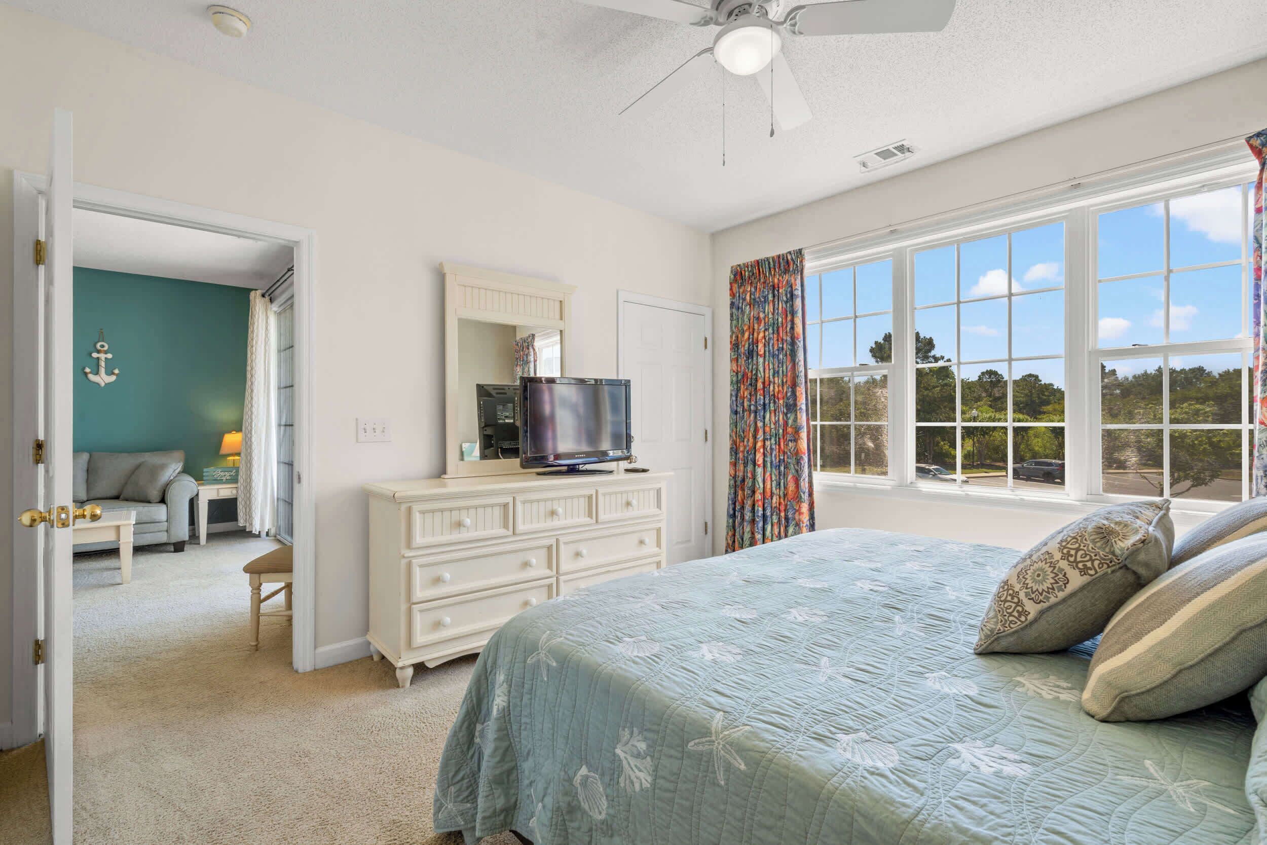 Un dormitorio con cama, cómoda, televisor y vistas al exterior.