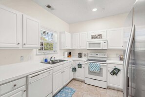 A kitchen with white cabinets, a microwave, an oven, a dishwasher, and a refrigerator. - "Seas the Day" at barefoot resort in Ironwood (North Myrtle Beach)